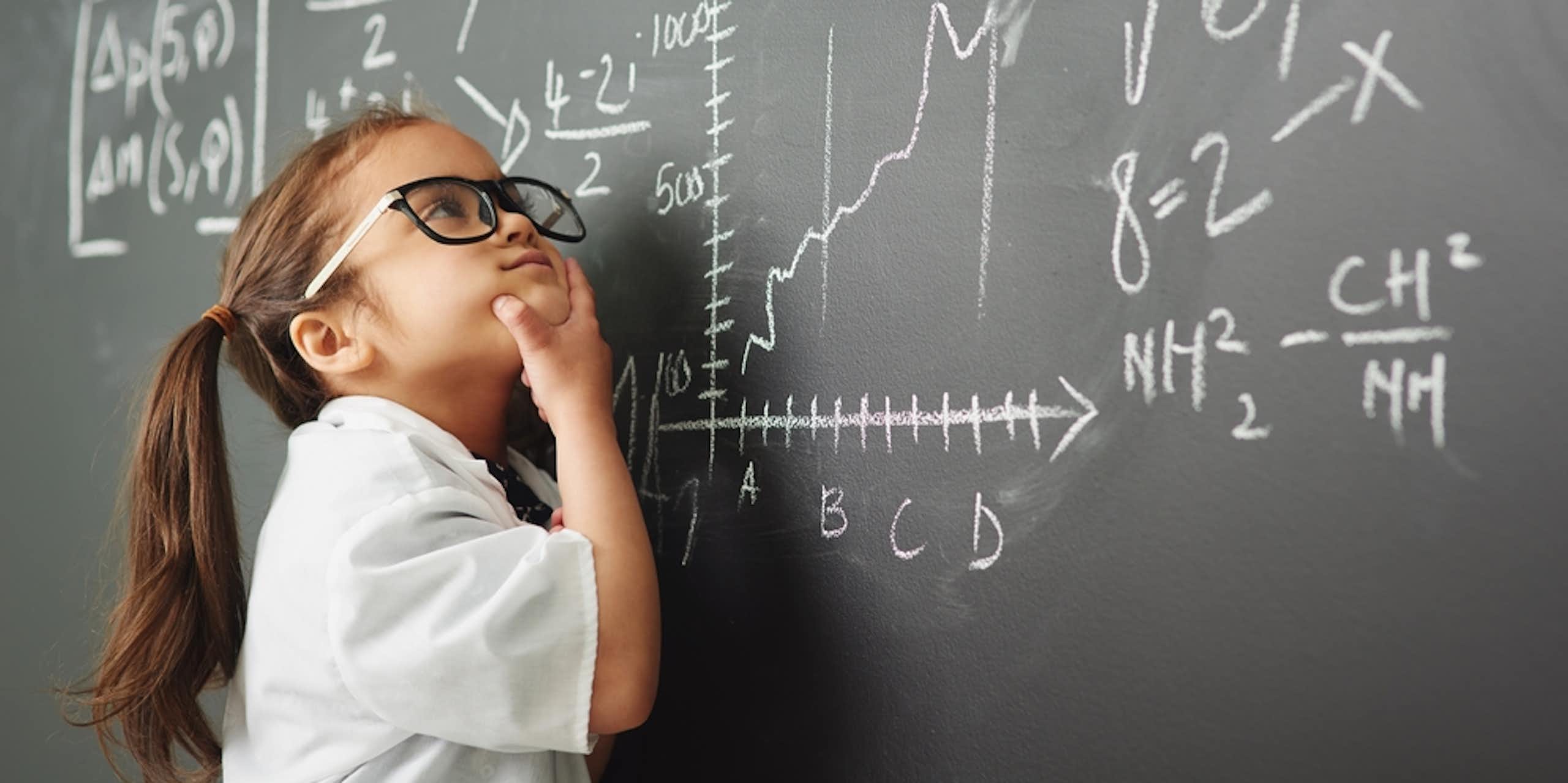 Petite fille avec des lunettes en train de résoudre des équations très compliquées sur un tableau noir dans une classe