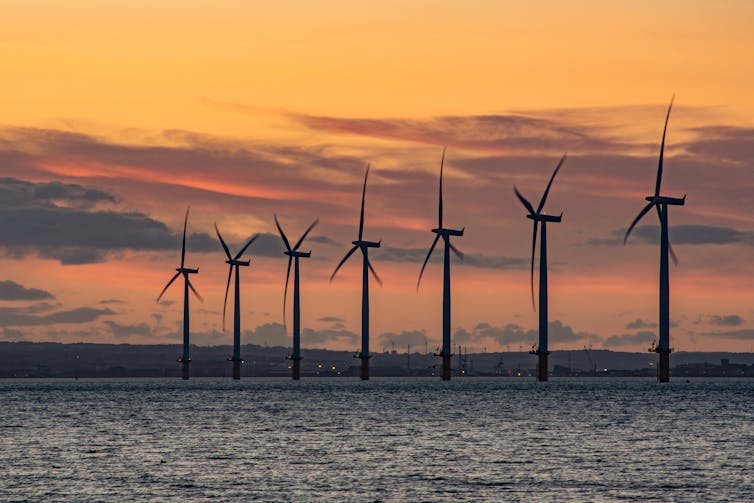 Wind turbines offshore at sunset.