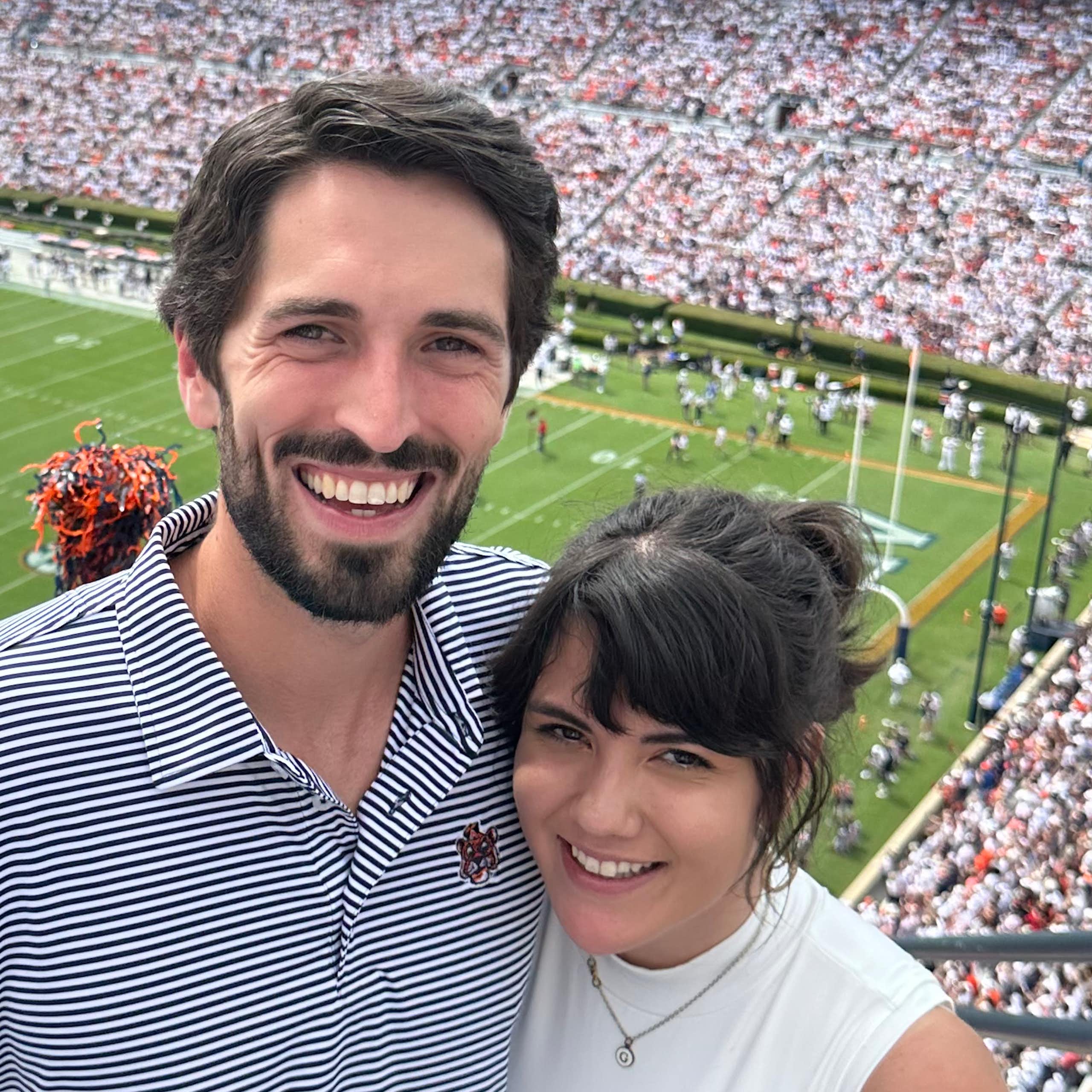 A smiling couple with a football stadium in the background.