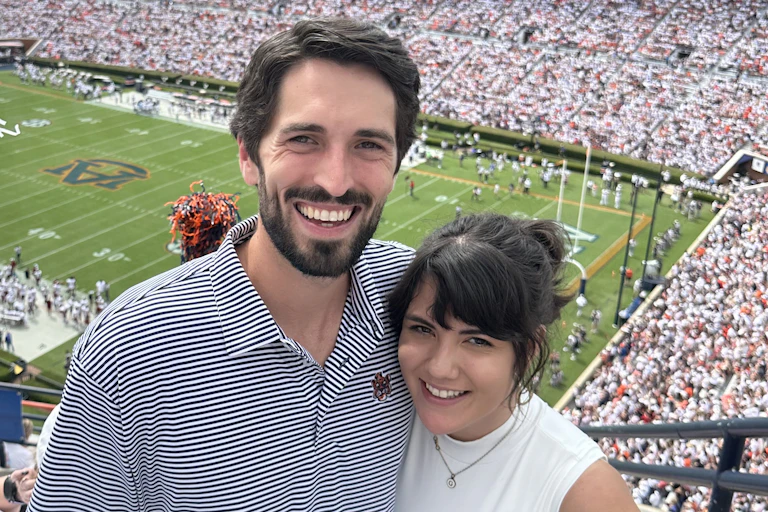 A smiling couple with a football stadium in the background.