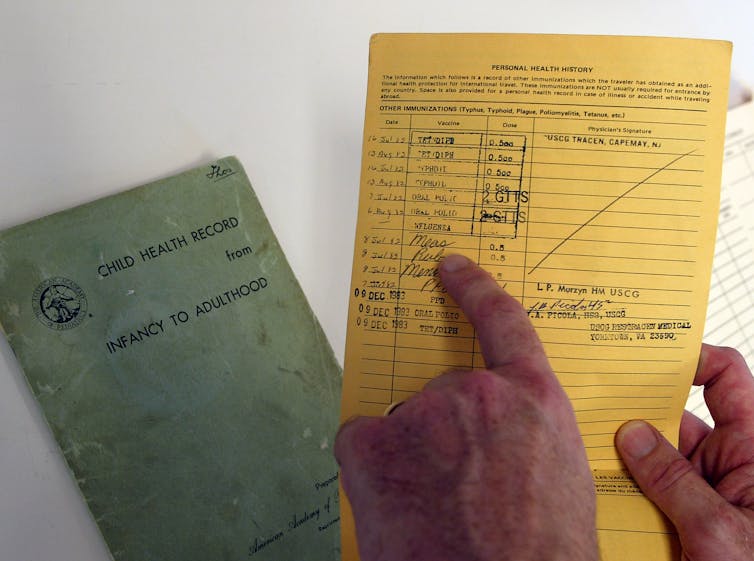 hands point to a handwritten vaccination record