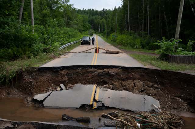 A collapsed road is seen with a person and vehicle in the background.