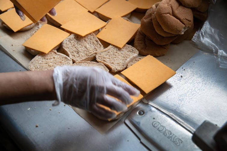 Gloved hand placing cheese slices on bun slices