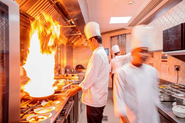 chefs in restaurant kitchen cooking wih flames