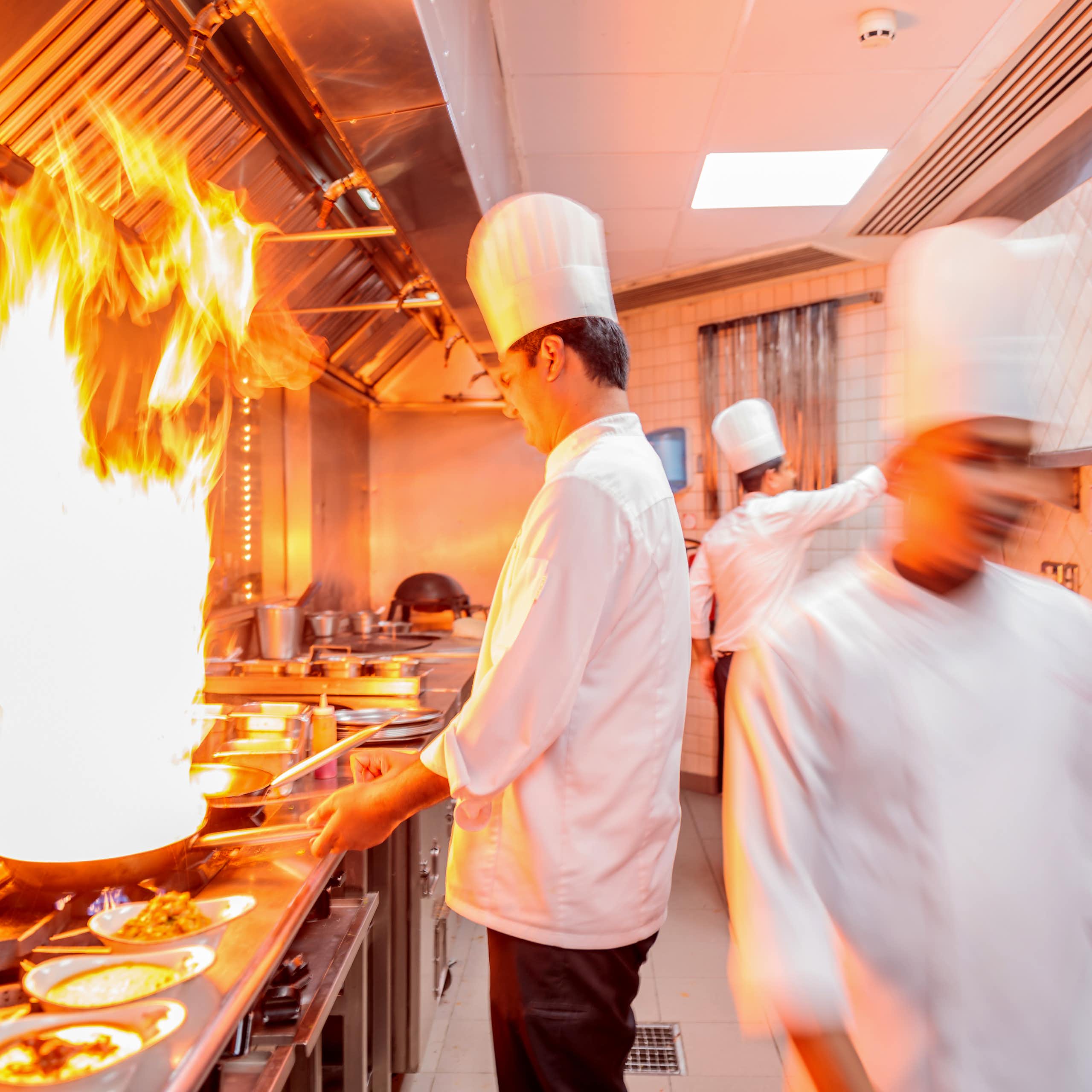 chefs in restaurant kitchen cooking wih flames
