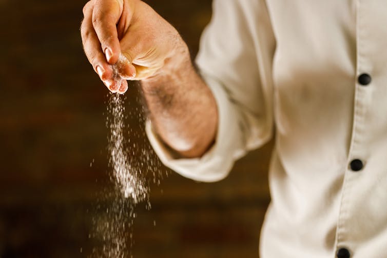 Close-up of a chef's hand dispensing a pinch of salt