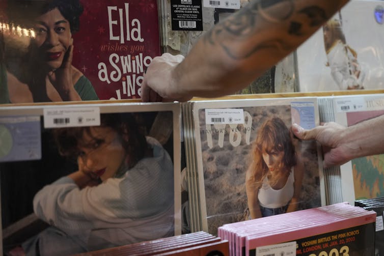 Tattooed arms peruse vinyl records featuring a young woman on the cover.