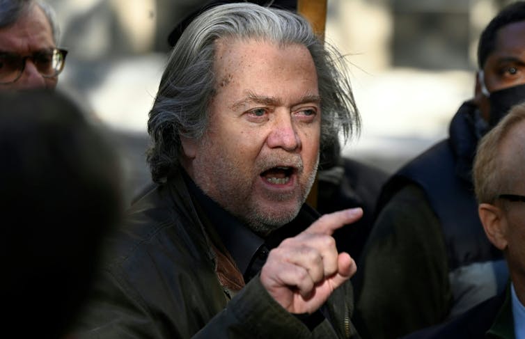 A man with long gray hair pointing his finger.