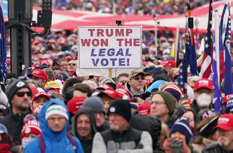 A large crowd of people with someone holding a sign that says 'Trump won the legal vote!'