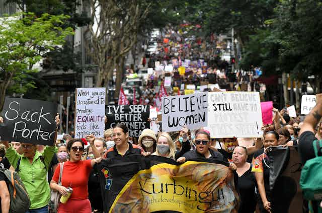 Mulheres carregando faixas com dizeres feministas se manifestando em uma rua 