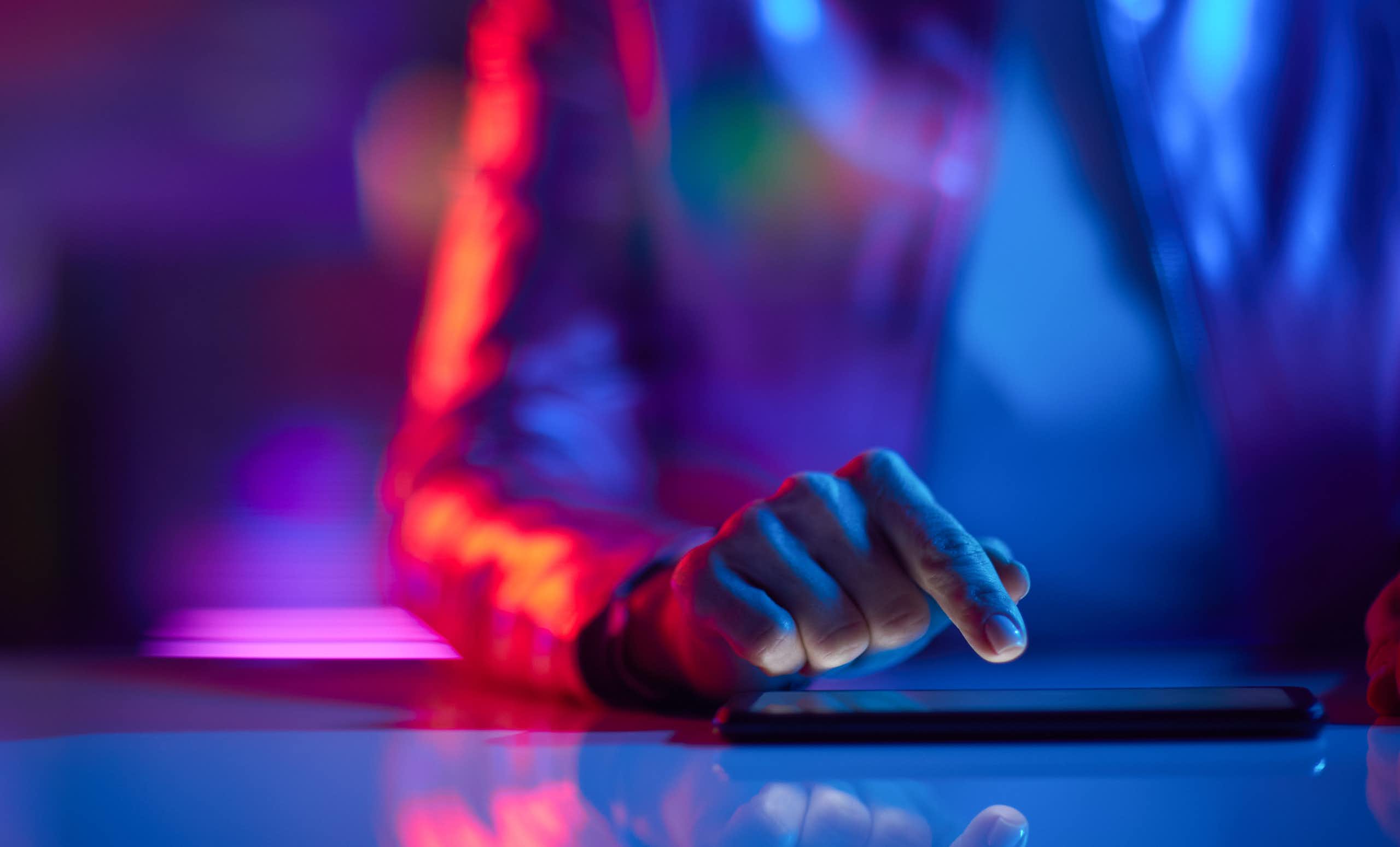 A red-blue lit image of a person tapping on a tablet device.