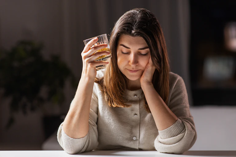Women looking down, palm on face, other hand holding tumbler