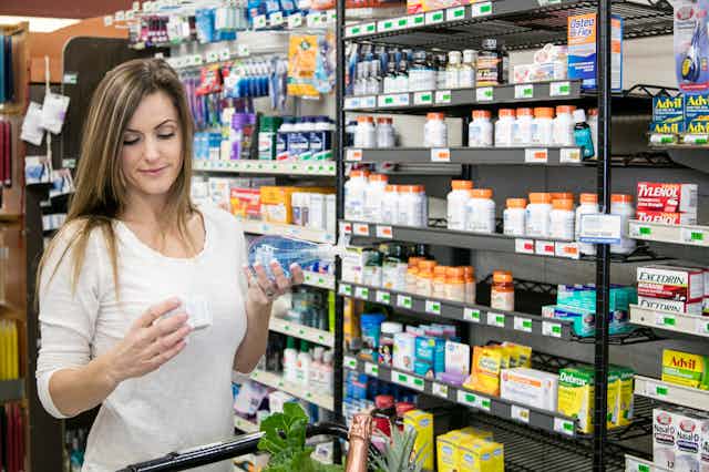 Woman reads label on a product in the pharmacy section of a grocery store.