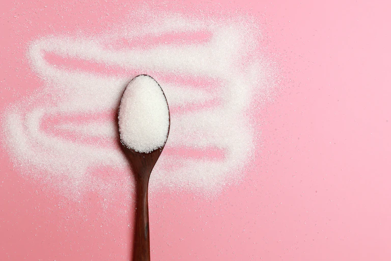 A spoonful of sugar on a pink background.