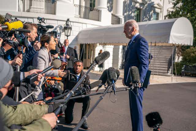 Joe Biden wearing a blue suit stands in front of members of the press.