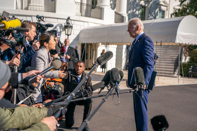 Joe Biden wearing a blue suit stands in front of members of the press.