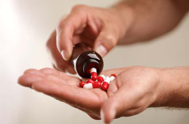 A person pours red and white tablets into their hand from a bottle.