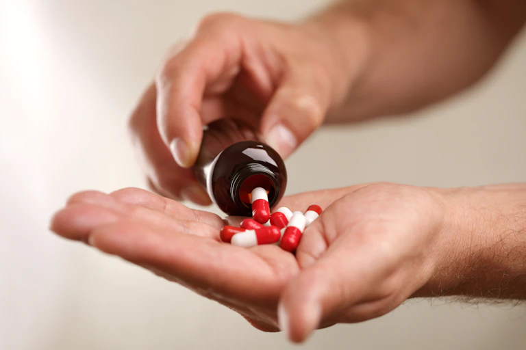 A person pours red and white tablets into their hand from a bottle.