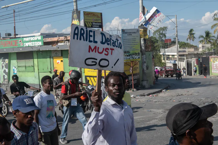 A group of people walking down a street holding a sign reading: