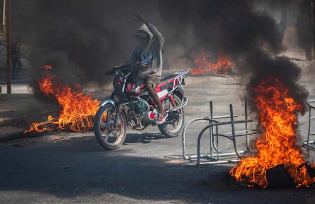 A person rides a motorcycle through street fires.