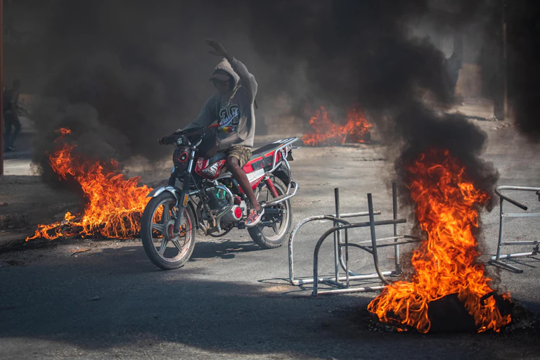 A person rides a motorcycle through street fires.