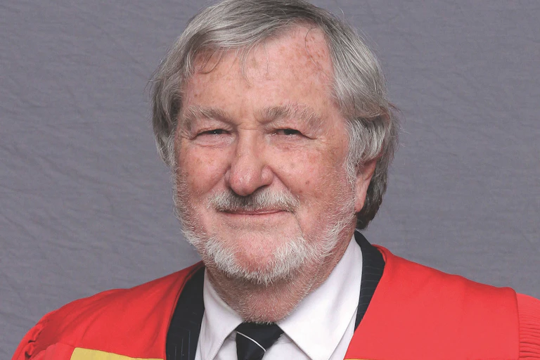 Head and shoulders portrait of a grey-haired man in academic gown