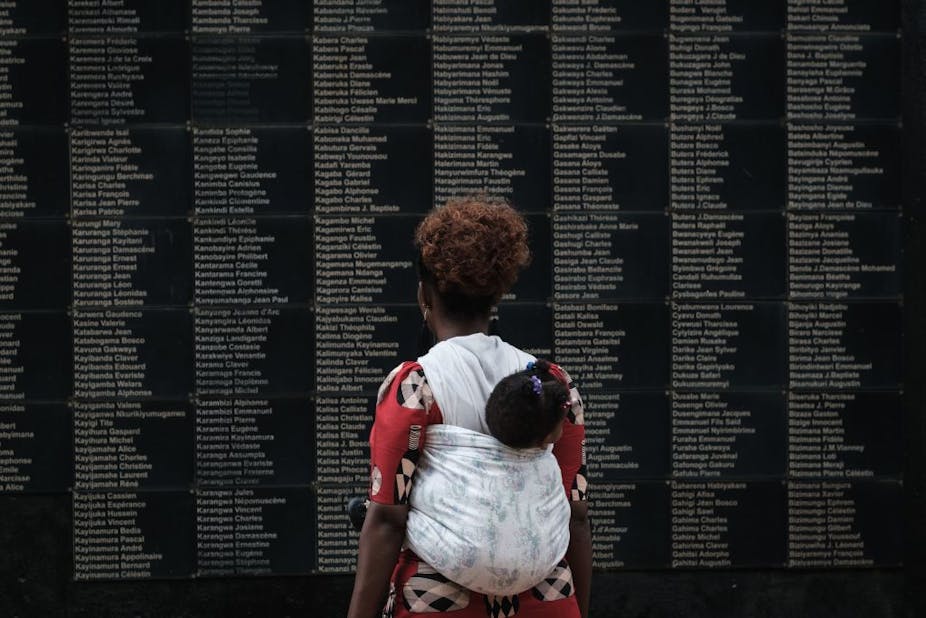 A woman standing in front of a black wall with white text on it, a baby strapped to her back