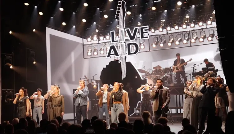 A group of actors singing on stage under bright lights.