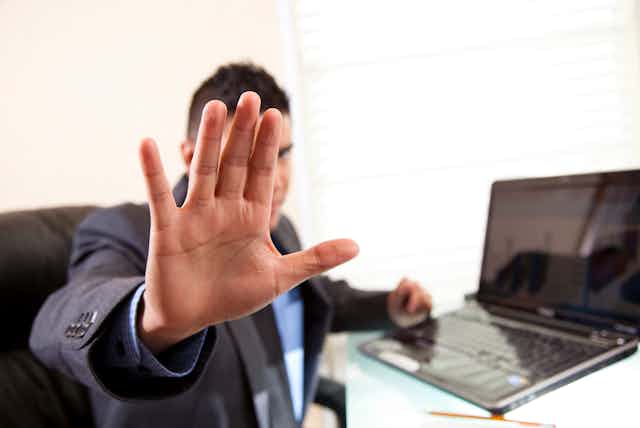 A person with his hand up blocking access to a computer.