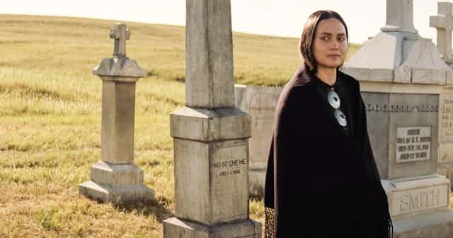 A Native American Osage woman standing in a graveyard in pale light. 