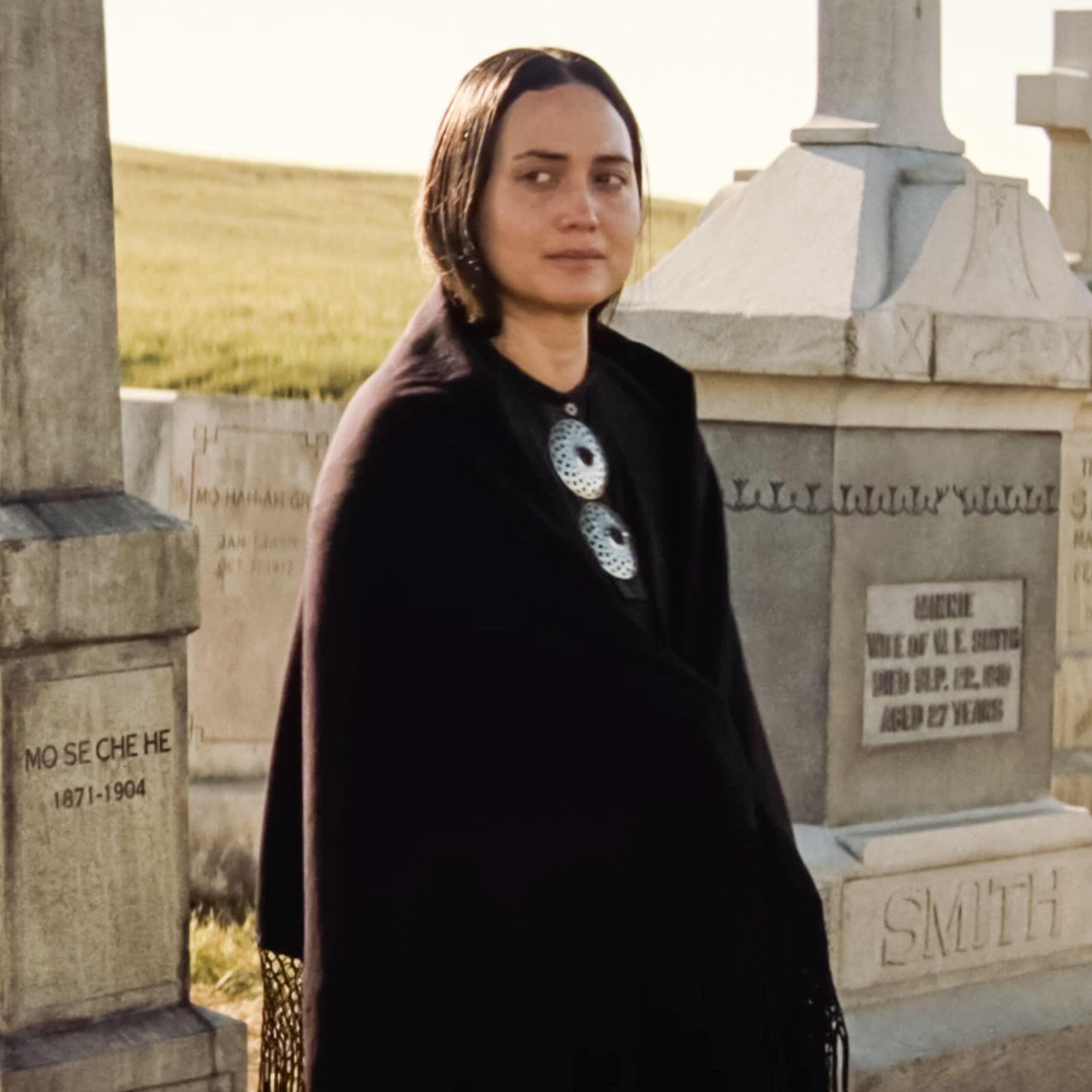 A Native American Osage woman standing in a graveyard in pale light. 