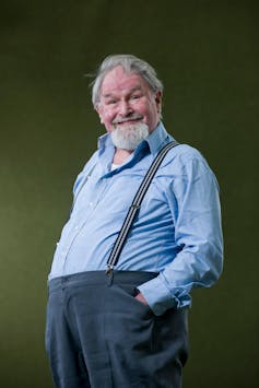 Wee old bearded man in braces smiling at the camera.
