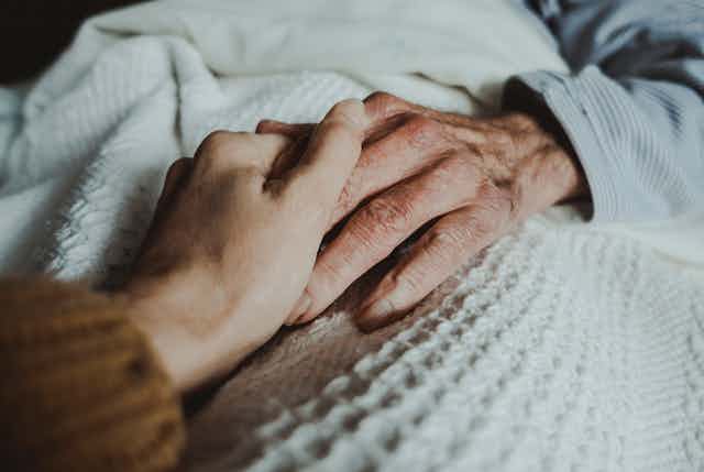 Two people's hands clasped on top of a white, textured blanket.