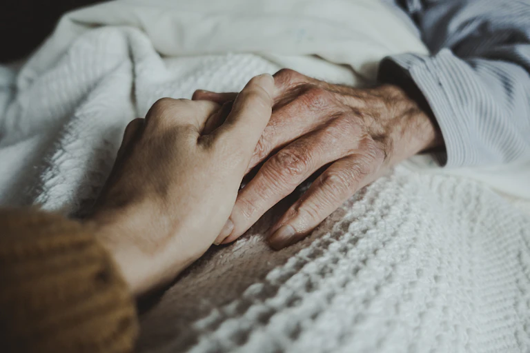 Two people's hands clasped on top of a white, textured blanket.