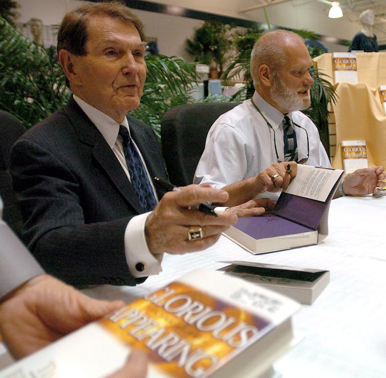 Two men seen sitting at a table with books.