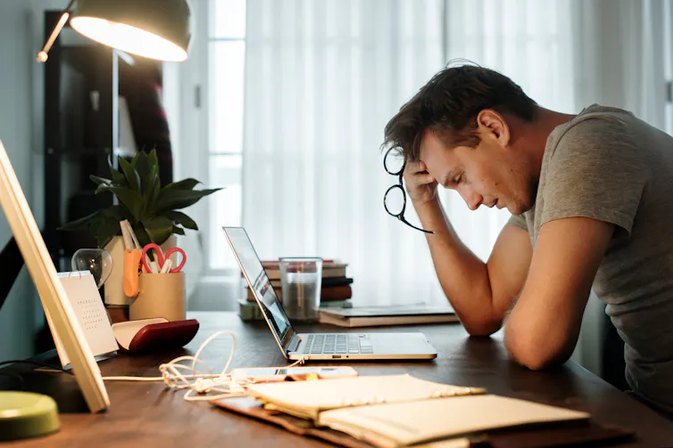 A man with a tired, stressed look on his face, rests his head against his hand while sitting at a desk