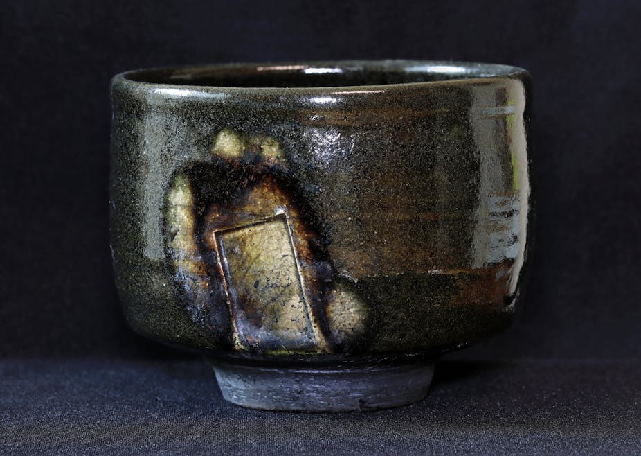 A gray, glazed bowl with brown and rusty sections, set against a dark background.