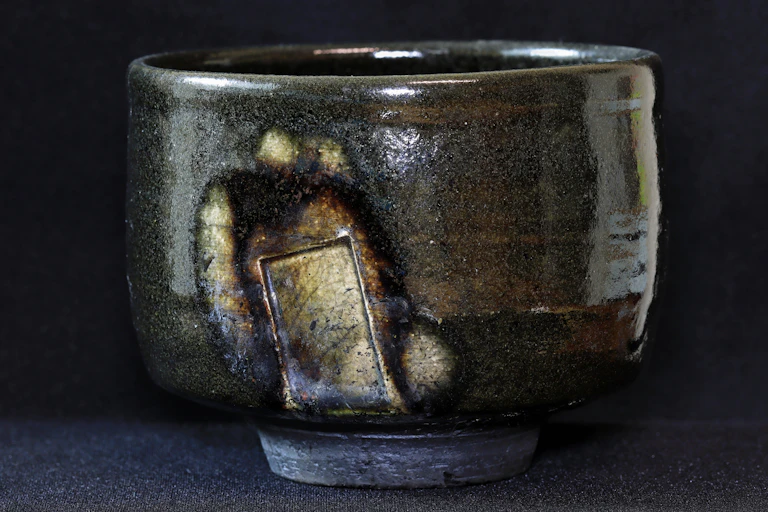 A gray, glazed bowl with brown and rusty sections, set against a dark background.