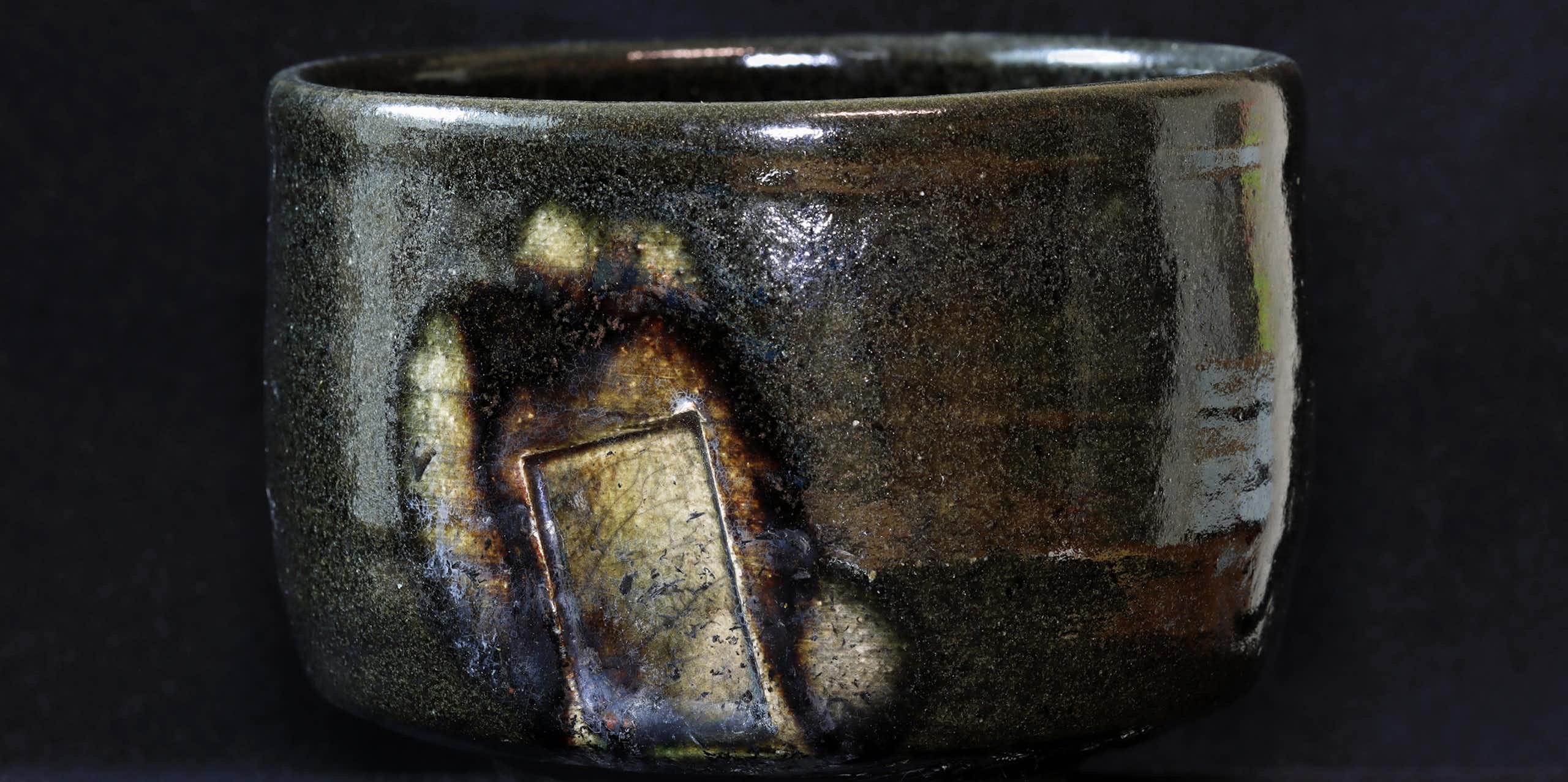 A gray, glazed bowl with brown and rusty sections, set against a dark background.
