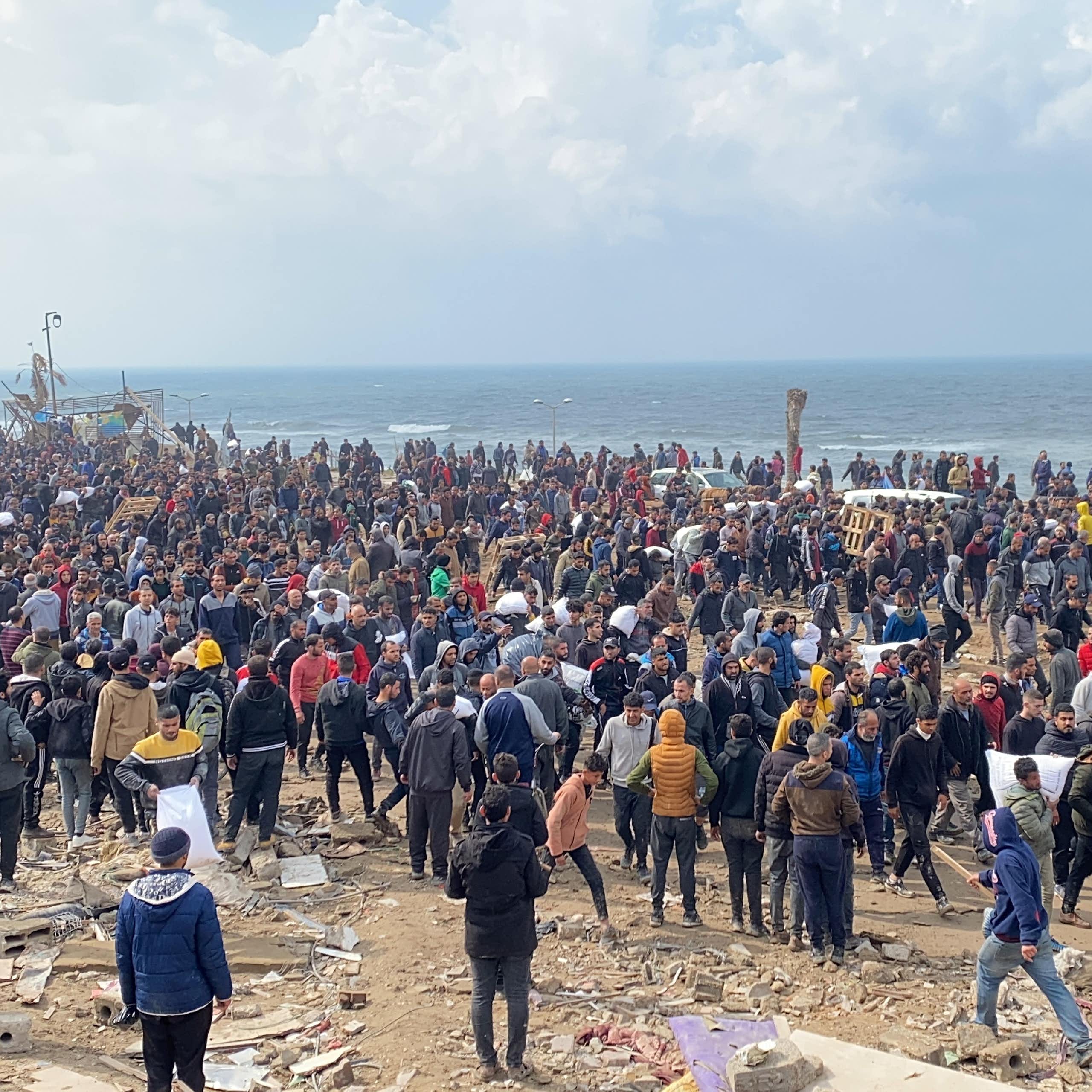 Hundreds of people gathered at a beach, which has rubble scattered around.
