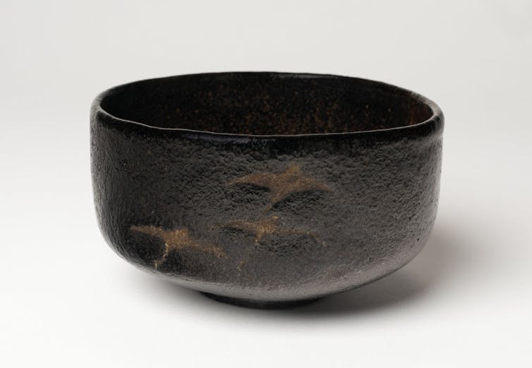 A plain black bowl with a faint golden pattern, resting against a white backdrop.