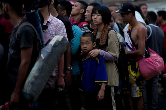A group of Chinese men, women and children line up, some carrying luggage.
