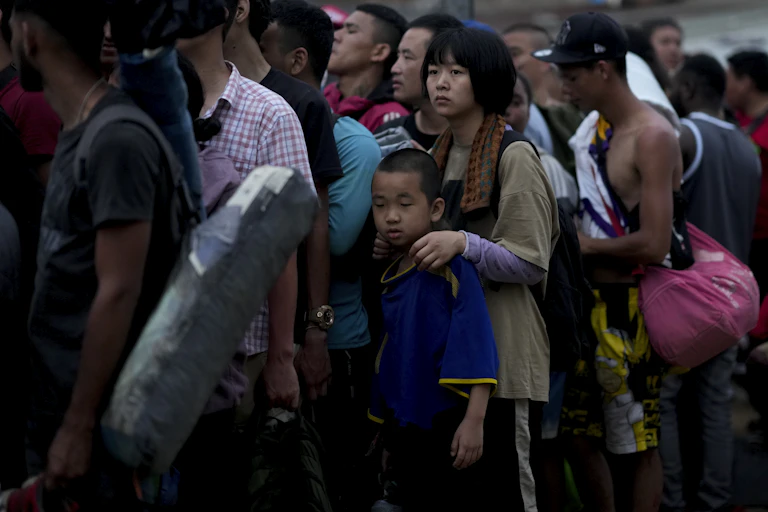 A group of Chinese men, women and children line up, some carrying luggage.