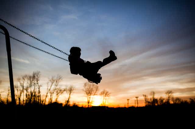silhouette of child on swing at sunset