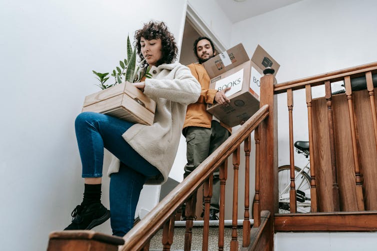 A man and a woman walk down stairs carrying boxes of books.