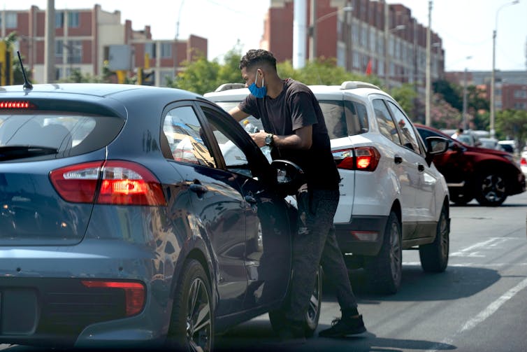 A man cleaning a car's windshield as it stops at a traffic light.