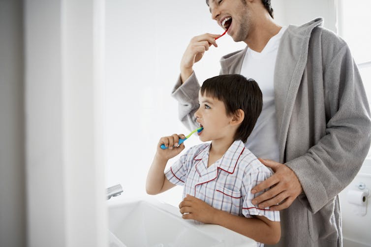 A father and his young son brush their teeth.
