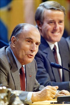 Two men smile as they sit behind microphones.