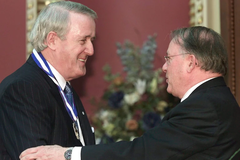 A man smiles as he shakes hands with another man.