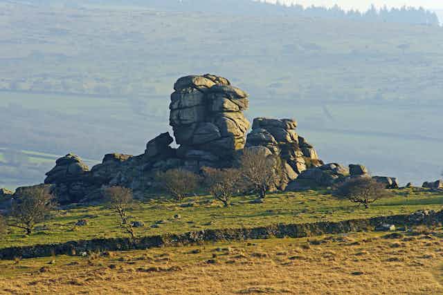 Green moorland with grey granite rocky outcrop in centre of frame, Dartmoor green fields in background